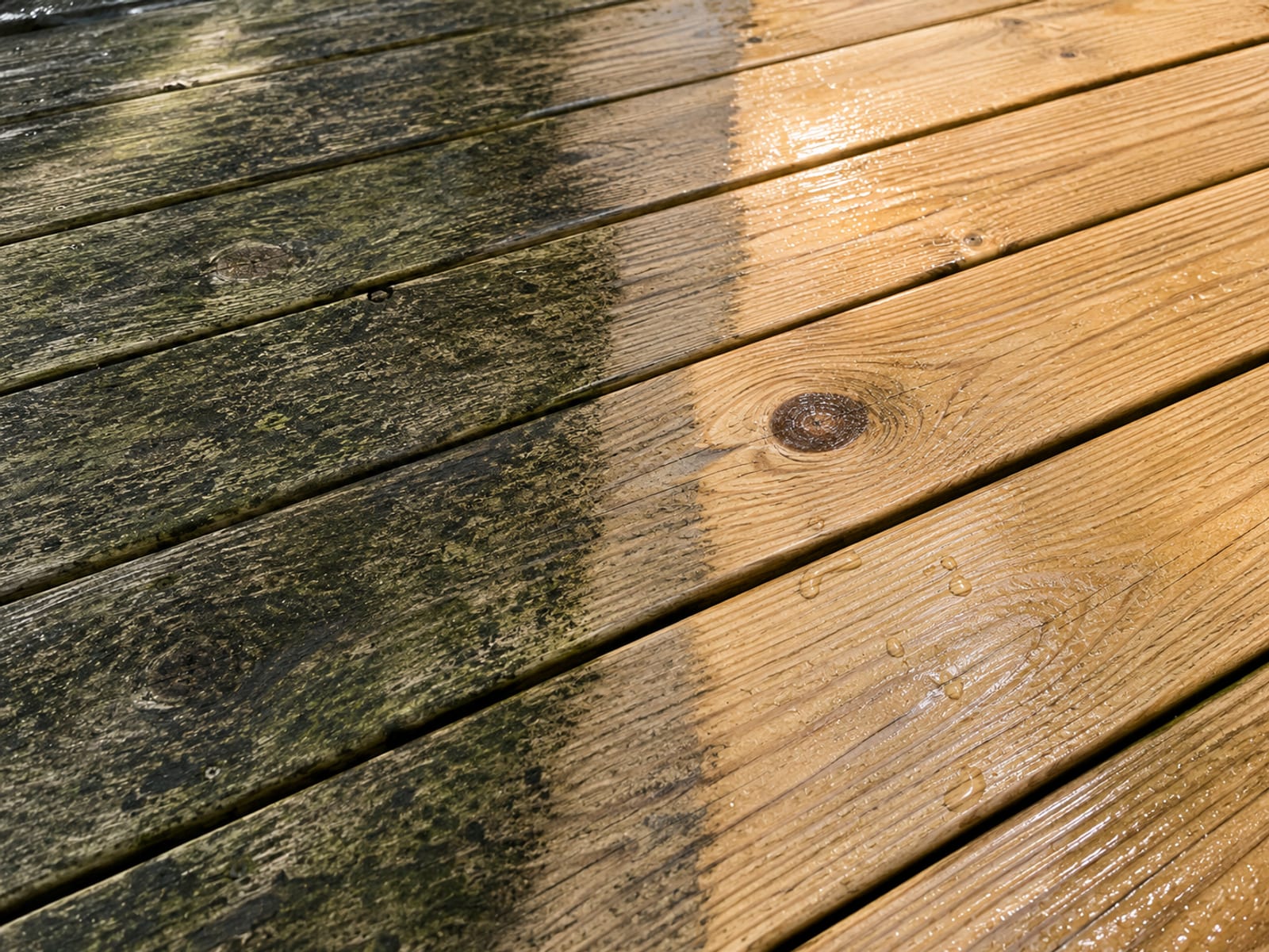 Close-up split-surface view of a weathered deck board edge transitioning sharply to a clean pressure-washed section revealing restored wood grain