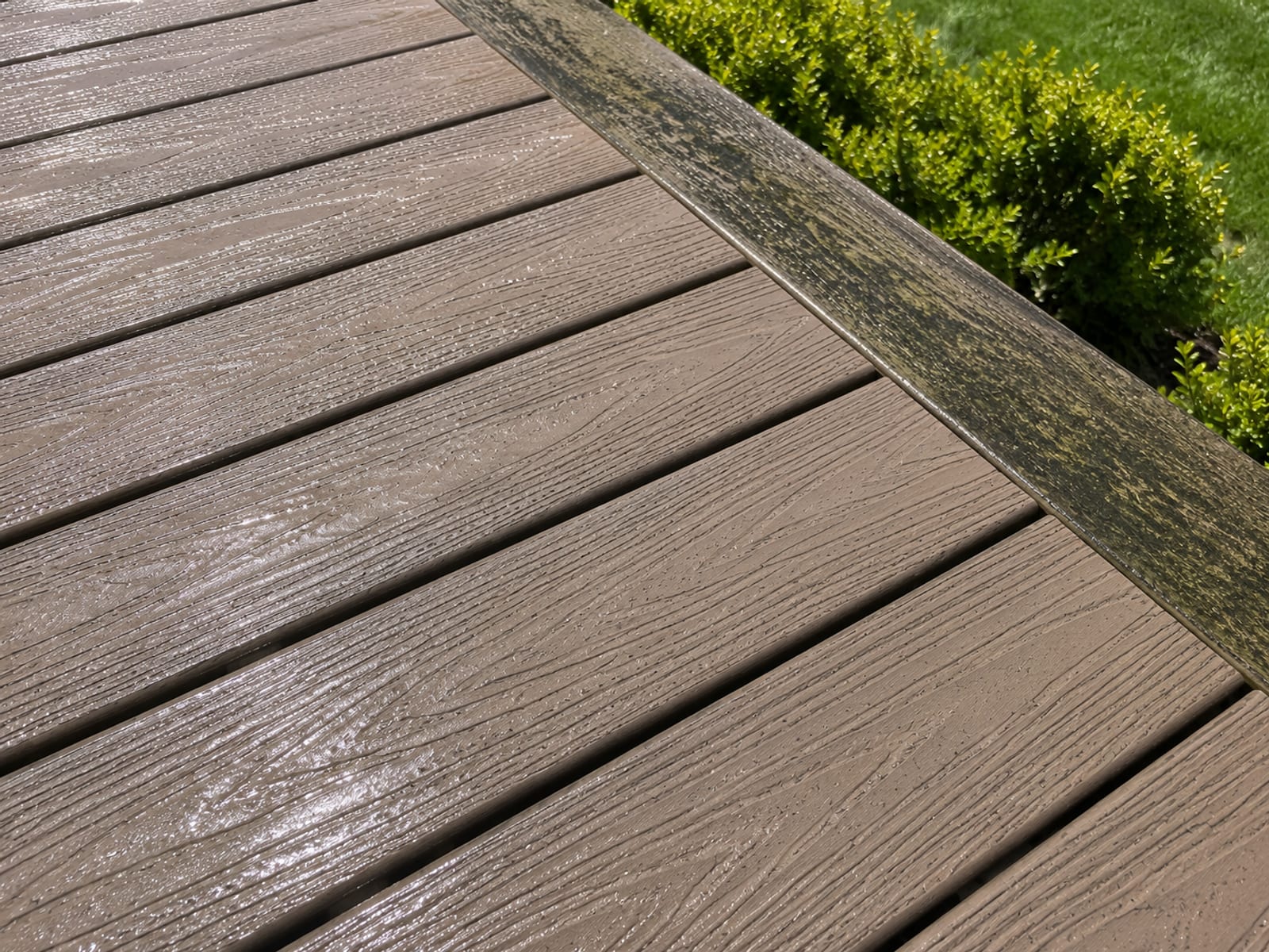 Close-up of a composite deck surface after pressure washing showing restored color and clean surface texture with damp sheen and surrounding green landscaping