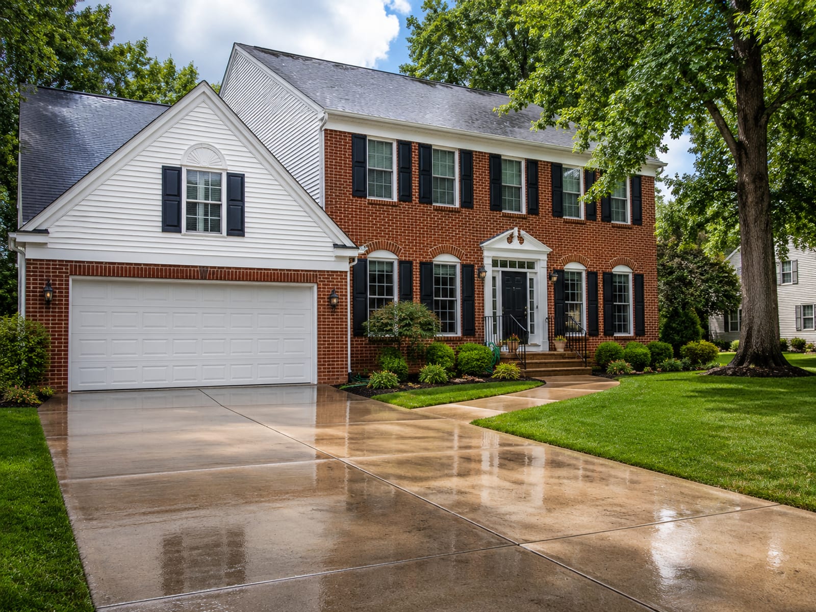 Wide view of a freshly pressure washed brick and vinyl sided colonial home with glistening wet surfaces and clean driveway