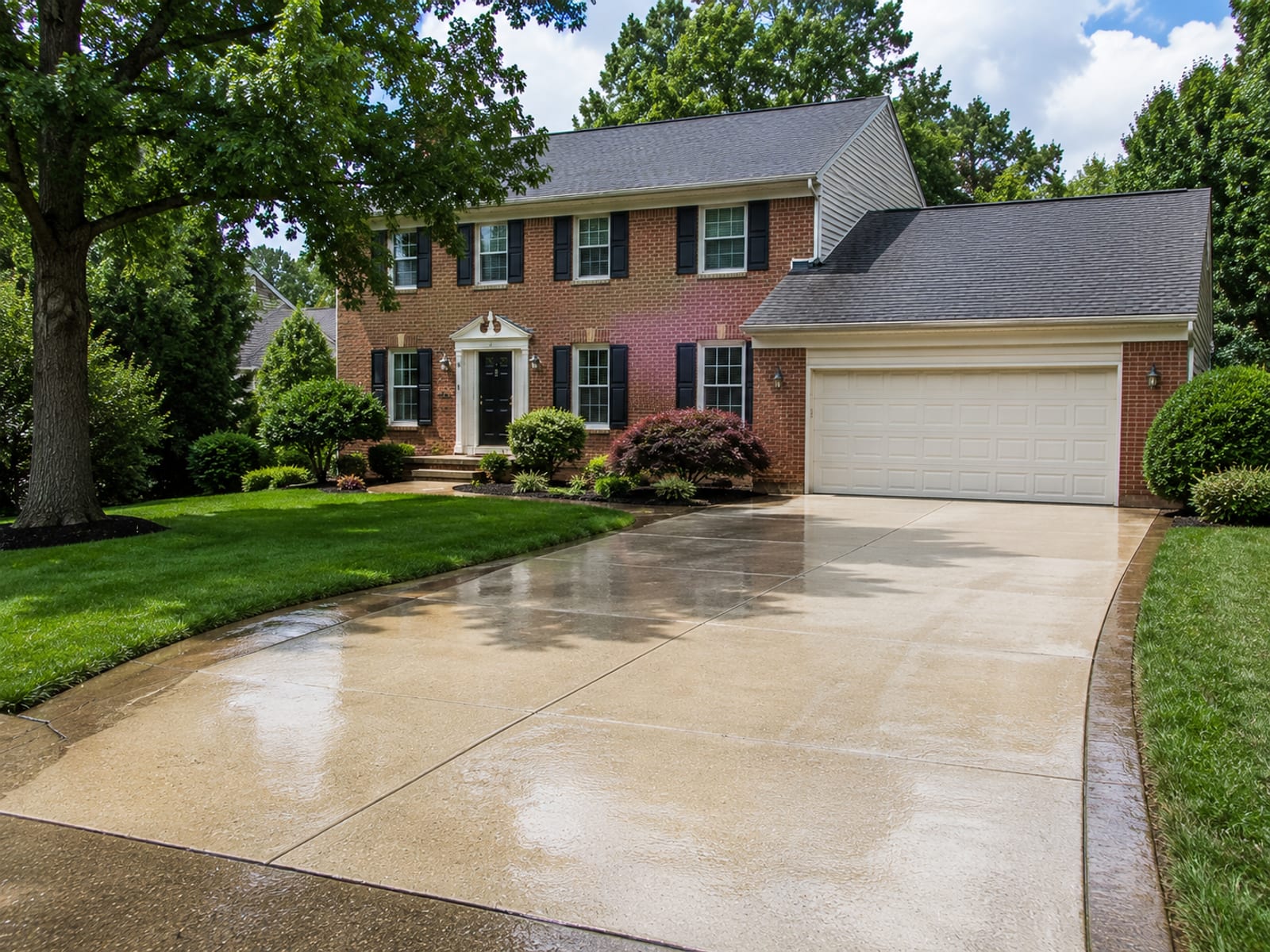 Wide view of a freshly pressure washed concrete driveway and brick colonial home exterior in a Catonsville Maryland suburban neighborhood