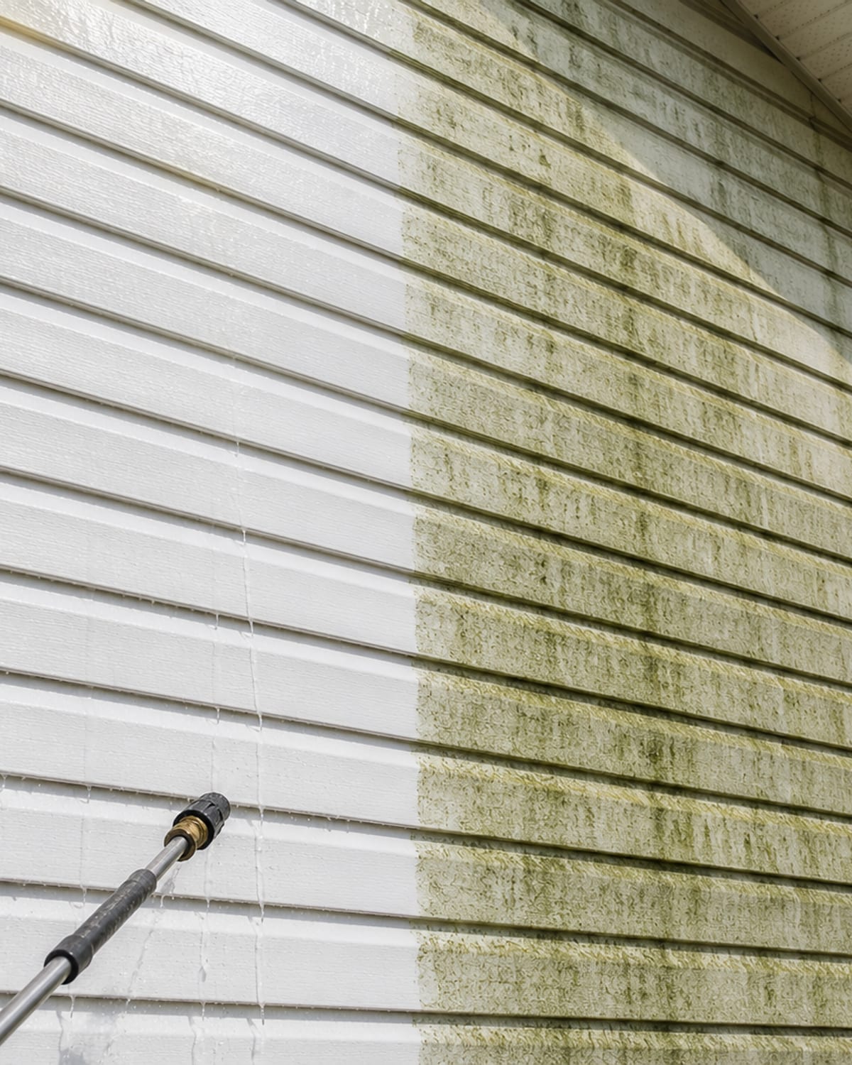 Angled close view of a mid-Atlantic vinyl sided home showing a stark contrast between freshly soft washed bright white siding and algae streaked dirty siding on the same wall in Catonsville Maryland