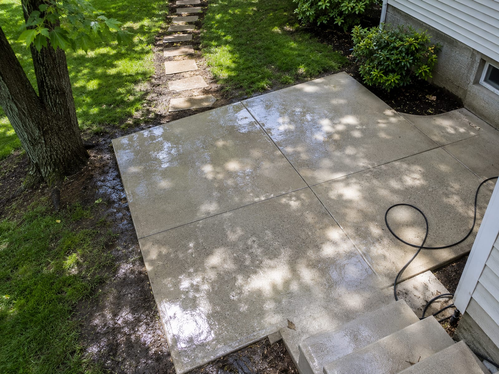 Overhead view of a freshly pressure washed concrete patio and stepping stone walkway behind a Baltimore County Maryland home showing bright clean surfaces surrounded by green grass and shaded by mature trees