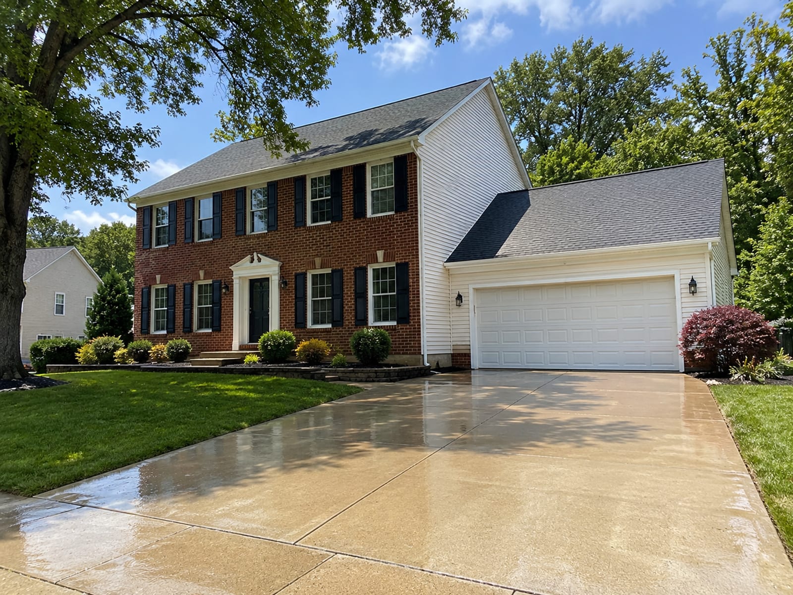 Wide view of a freshly pressure washed brick and vinyl-sided colonial home in a White Marsh Maryland suburb with clean driveway and lush green lawn