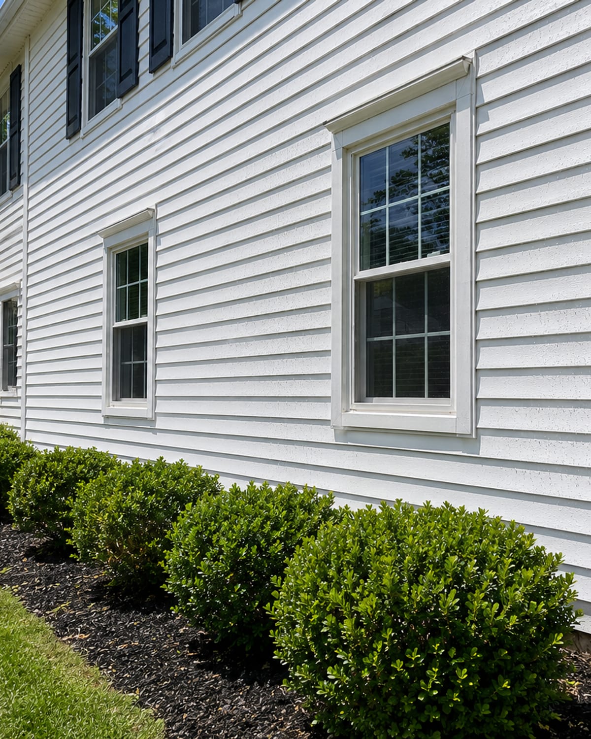 Close angled view of a freshly pressure washed white vinyl sided home exterior in a Woodlawn Maryland neighborhood showing clean bright siding panels with water droplets and green landscaping below