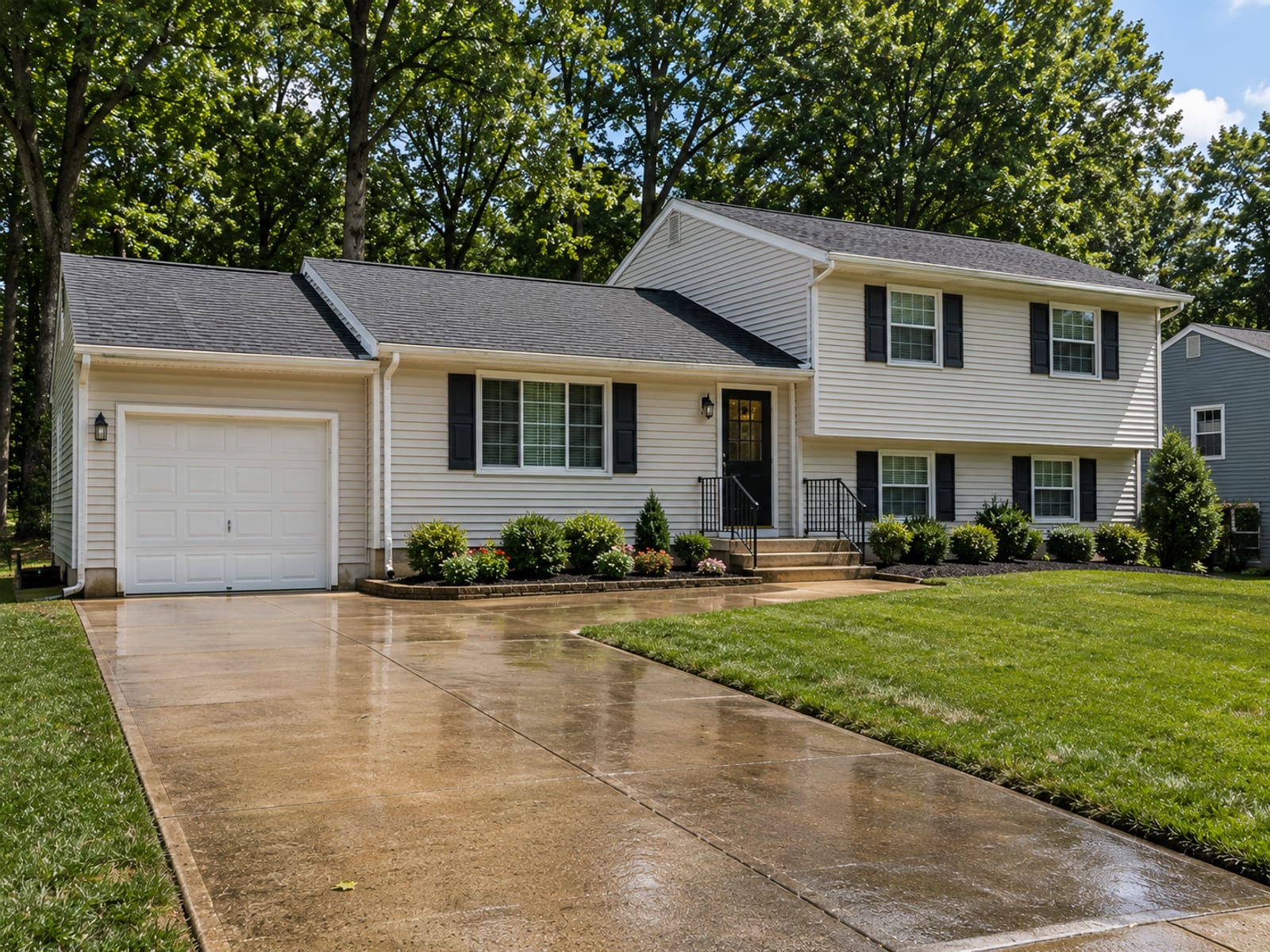 Close mid-distance view of a freshly washed vinyl-sided split-level home on a Baltimore County lot with clean driveway and damp concrete surfaces